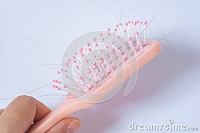 Hair loss problems with hand holding a pink hairbrush on white background. Falling black hair clinging to the comb Stock Photo
