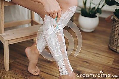 Hair Removal with depilation cream concept. Young woman in white towel applying shaving cream on her legs and holding plastic Stock Photo