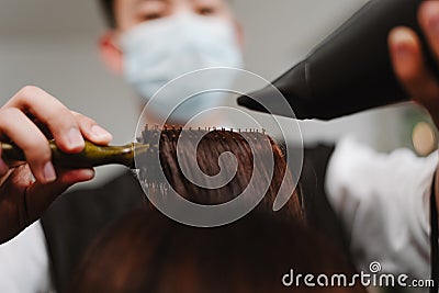 Hair salon concept a male hairstylist using a comb to grab a lock of hair and using hair dryer for drying and straightening Stock Photo