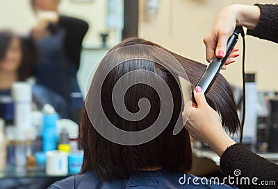 The hairdresser does aligns the hair with hair iron to a young girl, brunette in a beauty salon Stock Photo