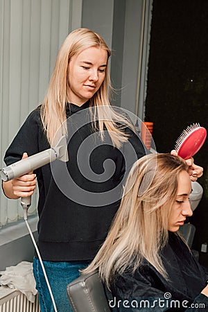 A hairdresser dries client& x27;s hair in salon. Hairdresser& x27;s hands with hair dryer Stock Photo