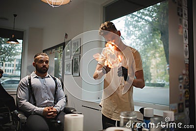 A delightful barber spraying fire flames with a hairspray and tools for beard shave on a barbershop background. Stock Photo