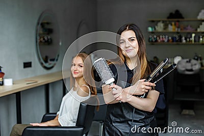 The hairdresser holds the brush and iron to straighten the hair. The client is sitting in a chair. Stock Photo