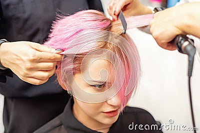 Hairdresser straights pink hair of woman by hair iron Stock Photo