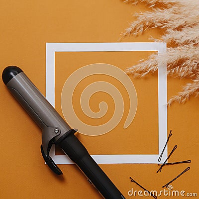 Hairdresser tools: curling iron and bobby pins over orange. Top view Stock Photo