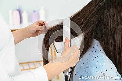 Hairdresser using modern flat iron to style client`s hair in salon Stock Photo