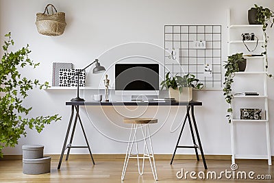 Hairpin stool standing by the wooden desk with mockup computer screen, metal lamp and coffee cup in real photo of white home offic Stock Photo