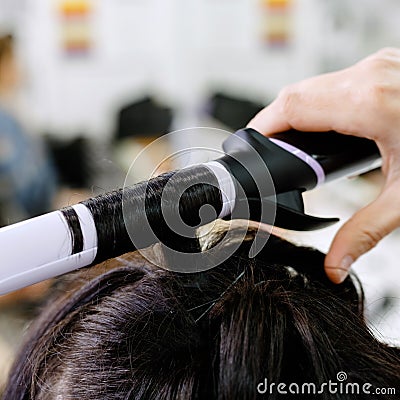 Hairstylist curling hair close up. Hairdresser making hairstyle to brown long hair woman in beauty salon. Professional hair care, Stock Photo