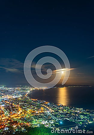 Hakodate City night view from Mt. Hakodate observatory, big bright moon light up the sea, golden reflection on surface Stock Photo