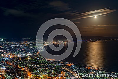 Hakodate City night view from Mt. Hakodate observatory, big bright moon light up the sea, golden reflection on surface Stock Photo