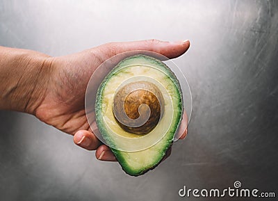 Half an avocado in a hand on the background of a steel table top view horizontal, fresh healthy food breakfast on kitchen, green Stock Photo