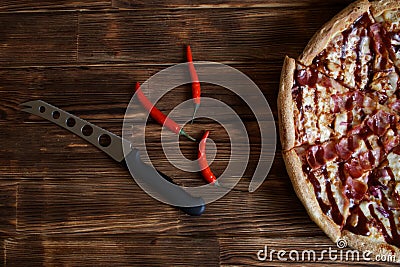 Half a barbecue pizza, red chili peppers and a cheese knife are natural wooden surfaces of pine planks Stock Photo