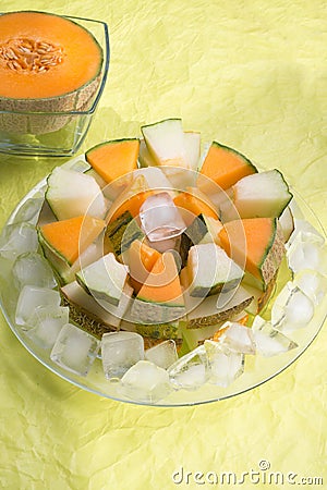 Half of cantaloupa melon and slices different melon with ice on plate around green background. tasty sweet exotic fruit Stock Photo