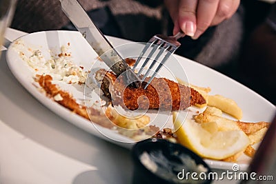 Half eaten fish and chips dish being cut using cutlery by a woma Stock Photo