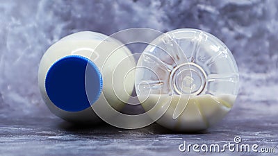 A half-empty and full plastic bottle of fresh regular milk lies on a dark gray marble or concrete backdrop. Close-up front view. Stock Photo