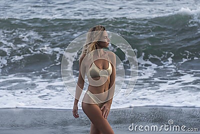 Half face shot of cute young woman in gold bikini on background of stormy ocean Stock Photo