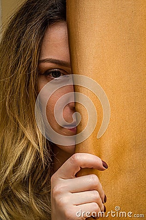 Half face of a young charming girl hidden behind a curtain Stock Photo