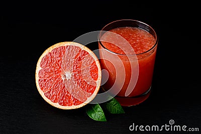 Half of fresh ripe grapefruit and glass of freshly squeezed grapefruit juice with pulp on black background. Low key image. Stock Photo