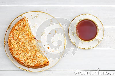 Half of homemade gooseberry pie garnished with almond petals and cup of tea on white wooden table. Stock Photo