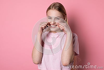 Half length portrait of beautiful blonde girl with blue eyes, wearing pink t-shirt, with fists near face Stock Photo