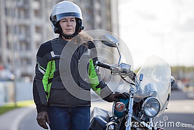 Half length portrait of female motorbiker in safety outfit standing near classic bike on urban streets Stock Photo