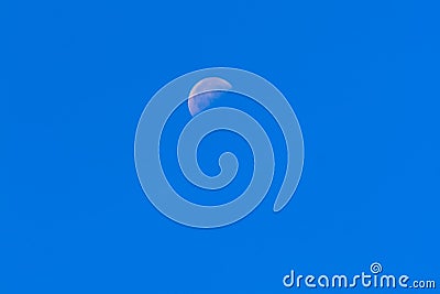 Half Moon During Day in Blue Sky. Bright moon orbiting earth in Stock Photo