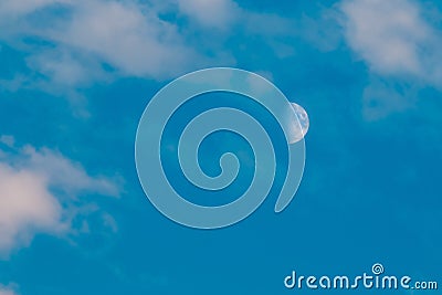 Half moon is seen in daytime, in blue sky with wispy clouds Stock Photo
