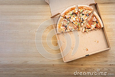 Half of sliced pizza in the cardboard box on the wooden table in restaurant. Top view and copy space for text Stock Photo