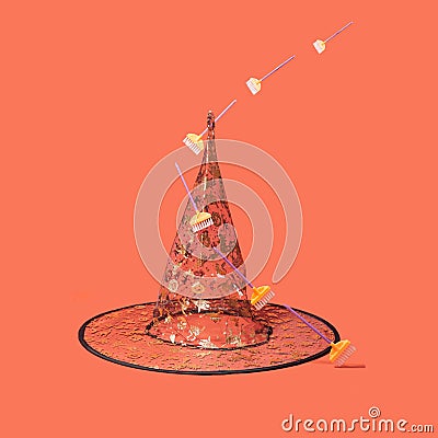 Halloween arrangement witch hat with golden glitter prints, broomsticks levitating around it. Minimal terracotta background Stock Photo