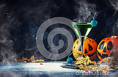 Halloween composition with festive drink, green cocktail and pumpkins lanterns, smoke and fallen leaves on night dark blue Stock Photo