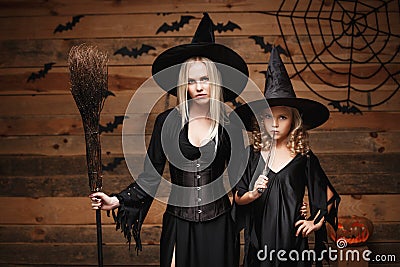 Halloween Concept - cheerful mother and her daughter in witch costumes celebrating Halloween posing with curved pumpkins over bats Stock Photo