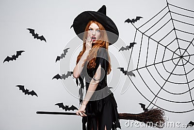 Halloween Concept - Happy elegant witch enjoy playing with broomstick halloween party over grey background. Stock Photo