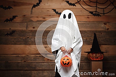 Halloween Concept - little white ghost with halloween pumpkin candy jar doing trick or treat with curved pumpkins over bats and sp Stock Photo