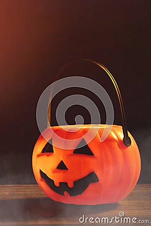 Halloween concept - Orange plastic pumpkin lantern on a dark wooden table with blurry sparkling light in the background, trick or Stock Photo