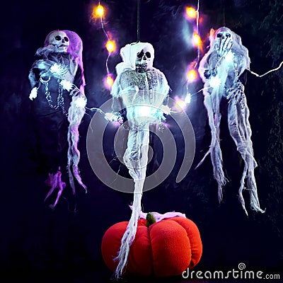Halloween decoration three skeletons in a multicolored cape decorated with a garland of glowing pumpkins and spiders. There is a Stock Photo