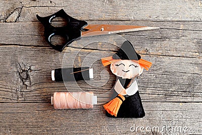 Halloween felt witch with broom, beige and black thread, needle, scissors on old wooden background. Tutorial. Step. Top view Stock Photo