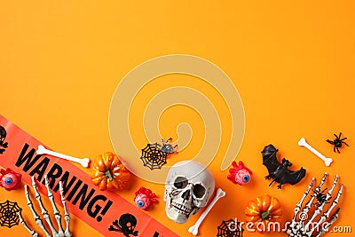 Halloween greeting card design. Flat lay, top view skull, spider webs, pumpkins, skeleton hands, warning tape on orange background Stock Photo