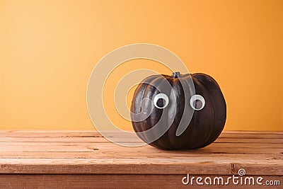 Halloween holiday creative concept with cute funny black pumpkin decor on wooden table over orange background Stock Photo