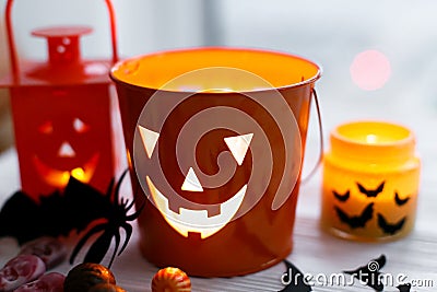 Halloween jack o lantern bucket, glowing candle, festive candy, skulls, black bats, ghost, spider decorations on white wooden Stock Photo