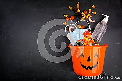 Halloween Jack o Lantern pail with spilling candy and COVID 19 prevention supplies over a black background Stock Photo