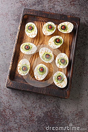 Halloween Monster eyes deviled Eggs stuffed with avocado cream wooden tray. vertical top view Stock Photo