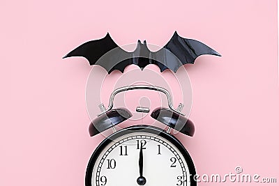 Halloween night concept. Black alarm clock and flying bat on pink background, closeup. Creative flat lay, top view, template for Stock Photo