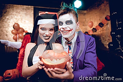 Halloween party. A guy in a Joker costume and a girl in a nun costume posing with a pumpkin-lamp. Stock Photo