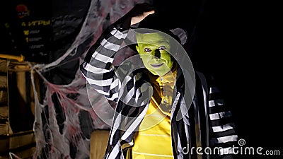 Halloween party, night, twilight, in the rays of light, a man with a terrible make-up, with a green face and a hat lifts Stock Photo