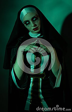 Halloween. Portrait of a scary devilish nun eyes looking at camera on a black and green background. Stock Photo