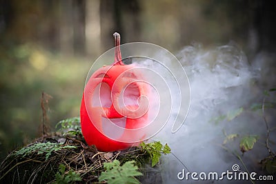 Halloween pumpkin in the autumn forest on an old stump. Jack lantern with steam from the mouth. In smoke or fog. Smoking or vaping Stock Photo