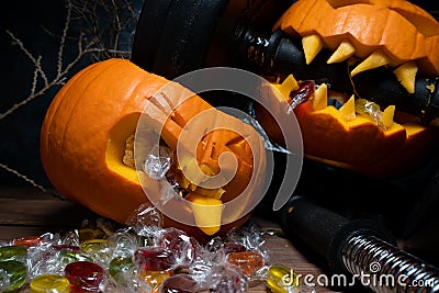 Halloween pumpkin clenching teeth on barbell dumbbell, crushing other carved Jack-o'-lantern. Stock Photo