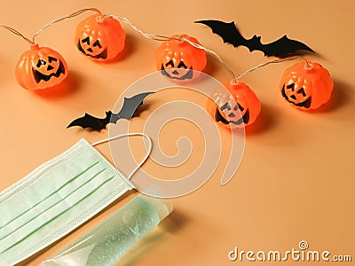 Halloween pumpkin lights , black paper bats,medical mask and alcohol sanitizer gel on orange background. Halloween , COVID-19 Stock Photo