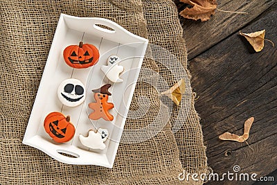 Halloween sweets lie in a wooden tray. Orange gingerbread in pumpkin shape and ghosts. Tasty cookie on table. Top view Stock Photo