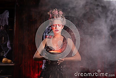 Halloween Witch with cauldron. Beautiful young woman conjuring, making witchcraft Stock Photo
